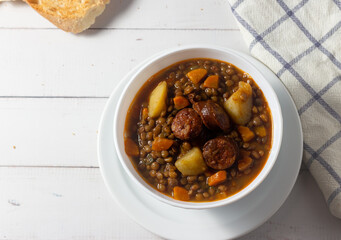 Traditional lentil soup with legs, carrots and chorizo on a white on a white background. Mediterranean cuisine.