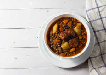 Traditional lentil soup with legs, carrots and chorizo on a white on a white background. Mediterranean cuisine.