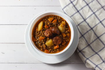 Traditional lentil soup with legs, carrots and chorizo on a white on a white background. Mediterranean cuisine.