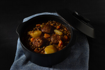 Traditional lentil soup with legs, carrots and chorizo on a black background . Mediterranean cuisine. Dark food