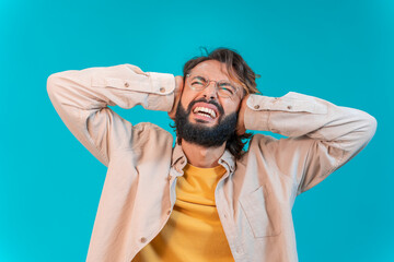 Stop noise. Young man standing over isolated background covering ears with annoyed expression for the high blare of loud music