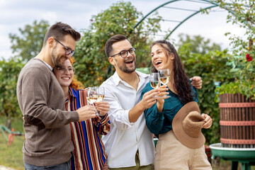 Four friends in vineyard talk to each other and smile with glass of vine in hands