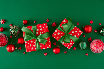 Christmas eve concept. Flat lay composition of red present boxes with green bows and red green baubles star ornaments on deep green background.