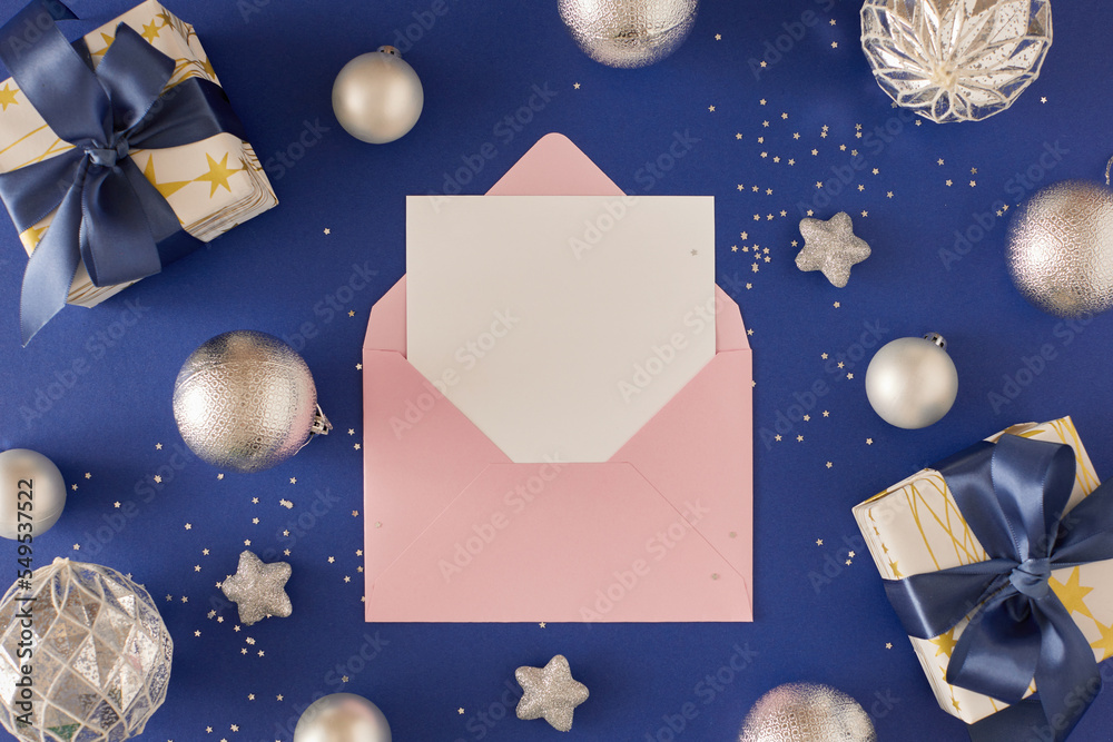 Wall mural New Year concept. Flat lay photo of present boxes with blue bows and Christmas baubles sequins silver stars on deep blue background with paper envelope. Creative holiday card idea.