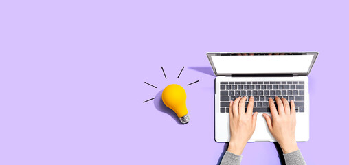 Person using a laptop computer and a light bulb - Flat lay - obrazy, fototapety, plakaty