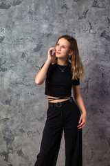 Obraz na płótnie Canvas Portrait teenager girl in stylish black clothes looking up away at grey textured studio background. Smiling confident teen girl 12-13 years old posing. Fashion style concept. Copy text space