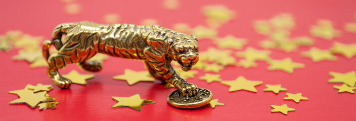 Banner with a bronze figure of a tiger with a coin on a red background and golden stars, copy space