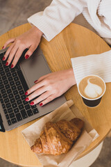 Pictures of women's hands holding a paper cup of coffee. Coffee to go concept. Top view of laptop computer. Freelance work.