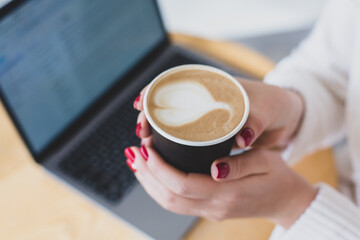 Pictures of women's hands holding a paper cup of coffee. Coffee to go concept. Top view of laptop computer. Freelance work.