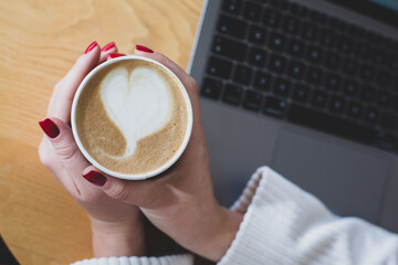 Pictures of women's hands holding a paper cup of coffee. Coffee to go concept. Top view of laptop computer. Freelance work.