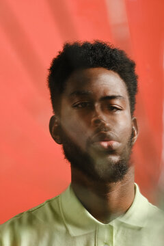 Vertical close-up cracked mirror effect studio portrait of confident young African American man standing against coral wall background looking at camera