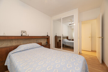 A room with a double bed with an elongated wooden headboard and a built-in wardrobe with sliding...
