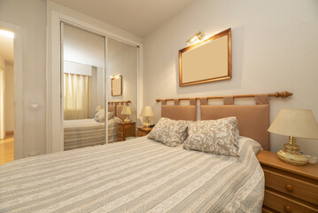 A room with a double bed with a wooden bar headboard and hanging cushions and a large white...