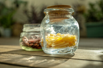 Some glass jars full of pasta with a cork stopper and another without a stopper and with dried chili peppers illuminated by a ray of morning sun