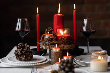 Rustic table decor for Christmas or New Year family dinner. Centrepiece with red candle, dry orange, cone, cinnamon, anise. Zero waste eco-friendly home. Cozy atmosphere, dark background. Close up