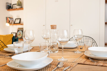 A wooden table with natural fiber placemats, crystal glasses and white porcelain dishes
