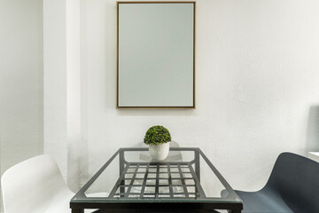 A square glass and metal table under a mirror and black and white resin chairs