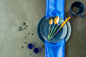 Top view image of various blue porcelain plates with blue tablecloth, gold-rimmed blue glasses,...