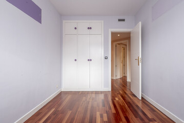 Empty bedroom with a three-section built-in wardrobe with matching trunks and round purple handles and a jatoba wood parquet floor