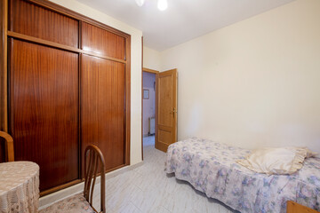 Bedroom with small bed with ugly patterned bedspread and large built-in wardrobe with sliding doors...