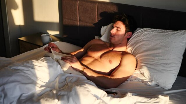 Young man shirtless on his bed reading a book