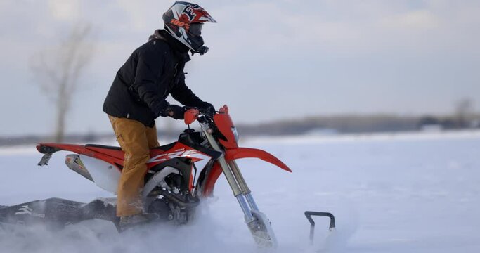 Man riding dirtbike snowmobile conversion through open field in winter - side profile - slow motion