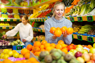 Smiling woman shopping for organic fruits in farmer store, choosing sweet ripe oranges ..
