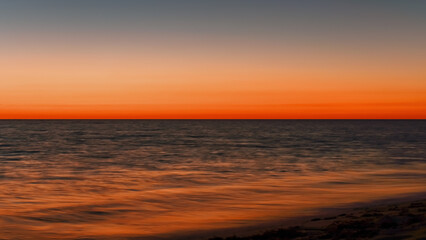 Obraz premium Vibrant orange red sky reflecting in calm ocean after sunset. Minimal landscape photo with space for text