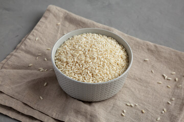 Raw Organic Carnaroli Rice in a Bowl on a gray background, side view.