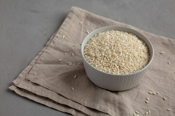 Raw Organic Carnaroli Rice in a Bowl on a gray surface, side view. Copy space.