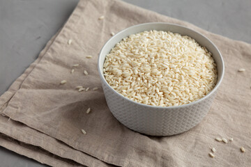 Raw Organic Carnaroli Rice in a Bowl on a gray surface, side view. Space for text.