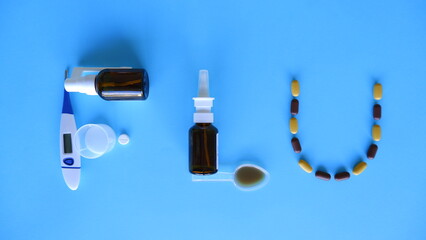 Flu word laid out of medications, pills, thermometer, traditional medicine for treating colds, flu, heat on a blue background. Maintenance of immunity. Seasonal diseases. Top view. Medicine flat lay