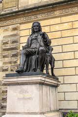 Copenhagen, Denmark - July 23, 2022: Closeup of Ludvig Holberg black statue on stone pedestal in front of Royal Theatre, yellow front facade