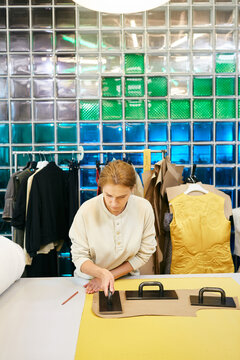 Mature Caucasian woman pressing paper pattern on bright yellow fabric vertical shot