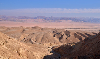 Fototapeta na wymiar Colorful landscape of a remote region in Negev Desert near kibbutz Yahel seen from a hiking trail. Panoramic view of orange sandy hills, mountain folds and dry wide wadi Ya'alon. Vacation in Israel.