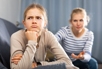 Sad female and daughter sitting at sofa and having quarrel at home