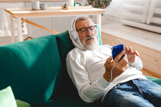 Senior hipster man using phone while listening playlist music on mobile app - Elderly male wearing face protective mask while watching video on smartphone