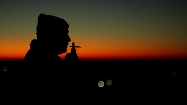 Silhouette of a man smoking a cigarette and thinking at sunset. It is a bad habit to smoke on the street in the morning. High quality 4k footage
