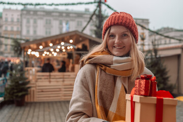 Stylish young beautiful happy woman walk with shopping bags and gift boxes on city street. Cheerful attractive girl shopper with paper bags and presents. Christmas shopping in mall. Winter sales. 