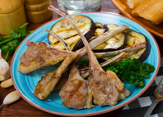 Grilled tasty lamb ribs with eggplants served at plate with greens on table
