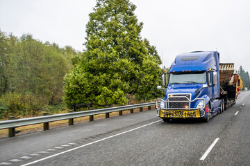 Obraz premium Heavy duty big rig blue semi truck tractor transporting oversized cargo on step down semi trailer running on the wide highway