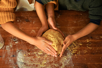 Children kneading cookie dough with their hands on a wooden table.