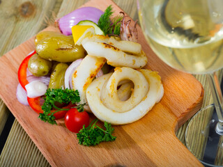 Baked calamari rings with potatoes and fresh vegetables and greens served with glass of white wine..
