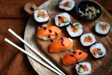 Sushi and rolls with avocado and salmon on a wooden board.