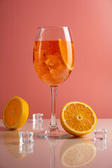 Glass of Aperol spritz cocktail on pink background.