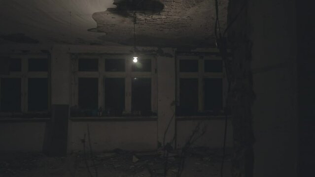 Lonely ordinary electric lamp hanging and swinging in the dark abandoned building. Smoke or steam on background of glowing light bulb. Steady gimbal shot