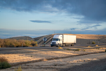 Fototapeta na wymiar Loaded long haul big rig white semi truck transporting cargo in reefer semi trailer running on the road in sunny time.