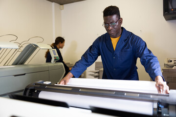 Attentive african american man uses plotter in small printing shop
