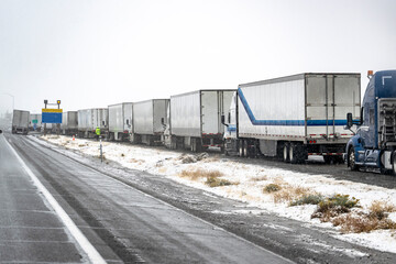 Long line of out of service big rigs semi trucks with loaded semi trailers standing on the highway shoulder due to a snow storm in the Lake Shasta area