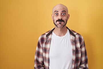 Obraz premium Hispanic man with beard standing over yellow background puffing cheeks with funny face. mouth inflated with air, crazy expression.